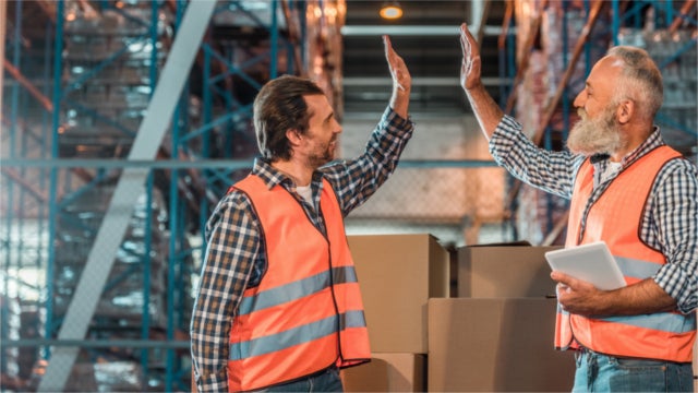 Two warehouse workers give each other a high five.