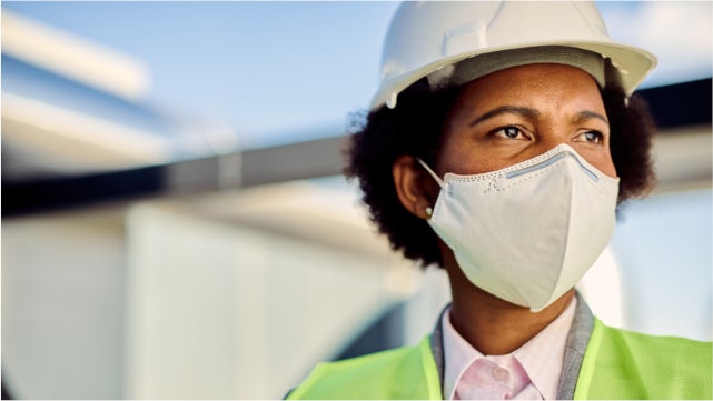 Black woman worker wearing a hard hat, reflector vest, and face mask.