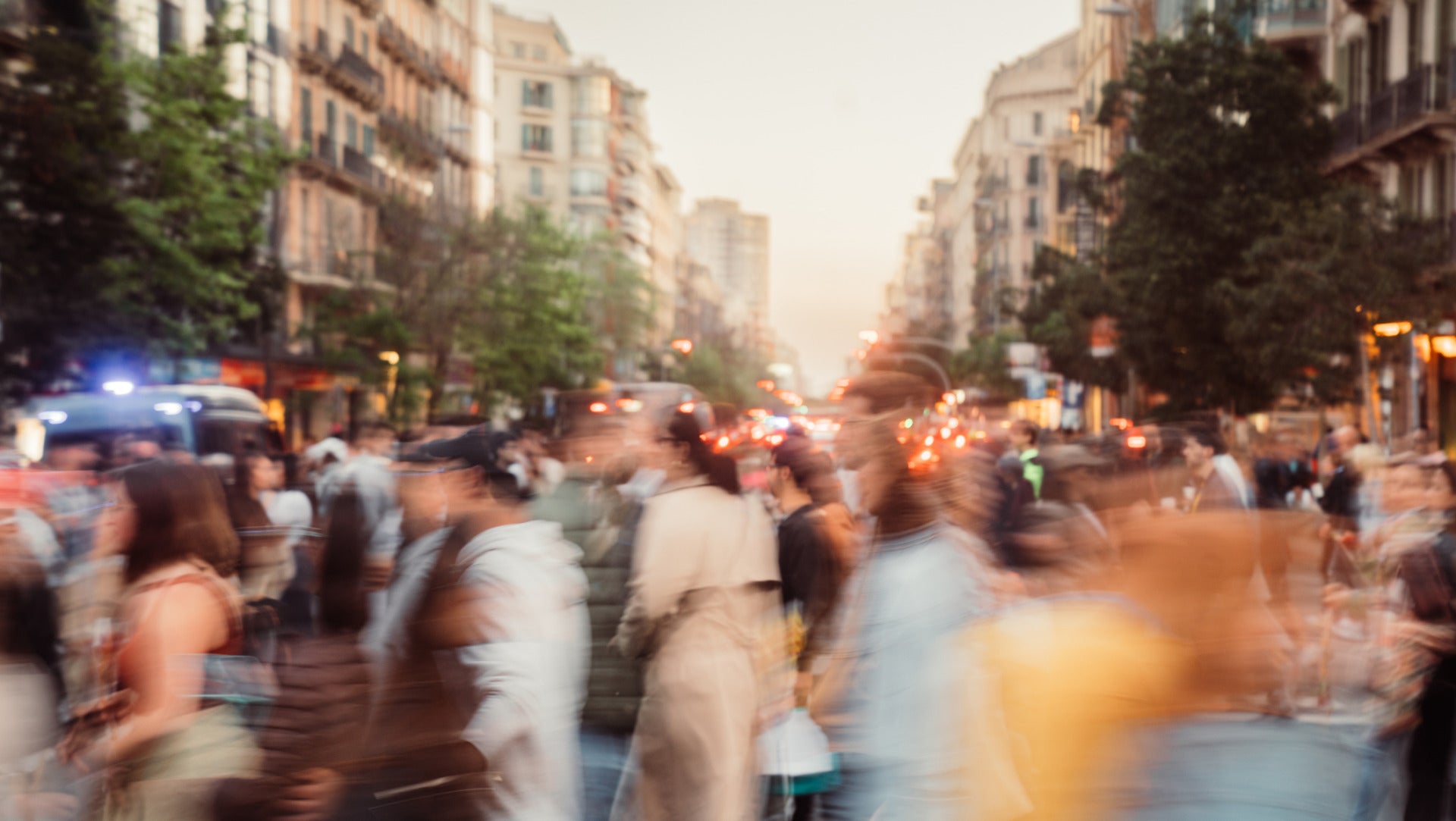 A photograph of a blurred crowd of people and cars on a busy city sidewalk.