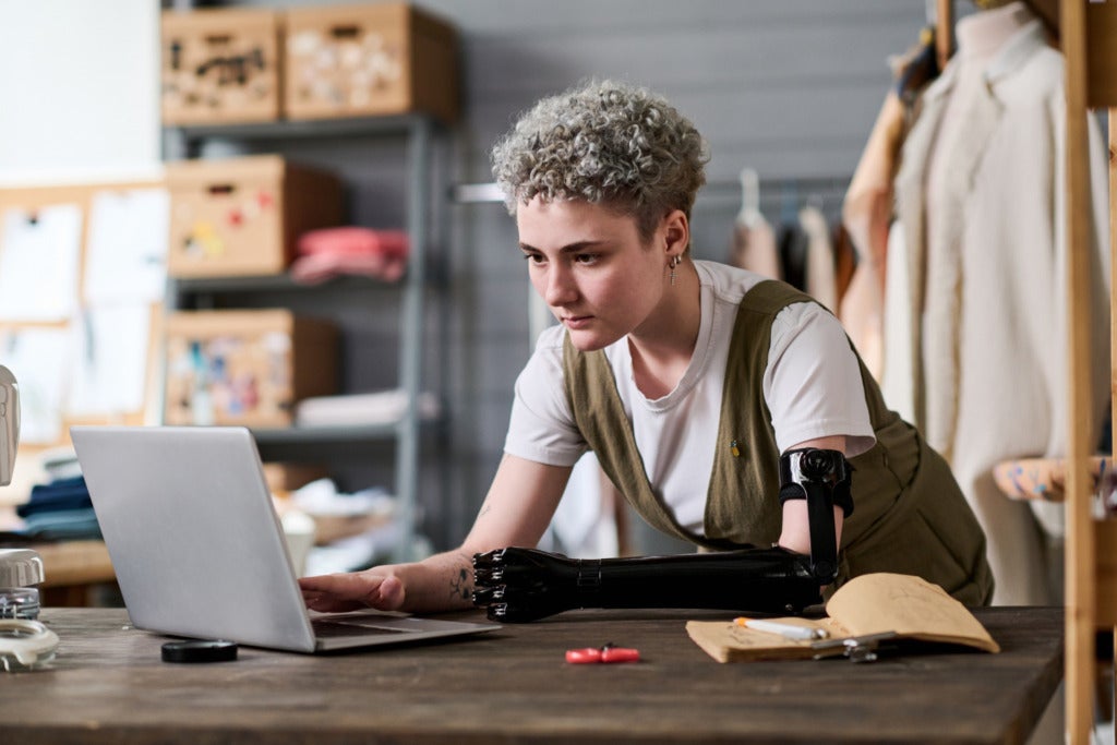 A young fashion designer with a prosthetic arm using a laptop.