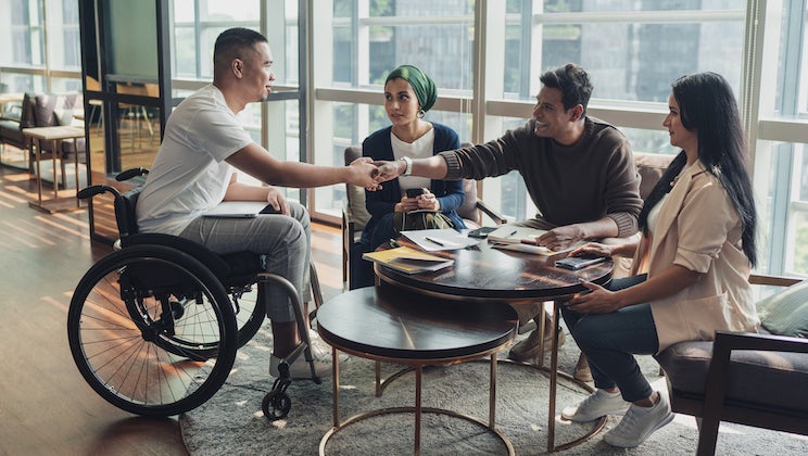 Three people in chairs and one person in a wheelchair sit around a table.