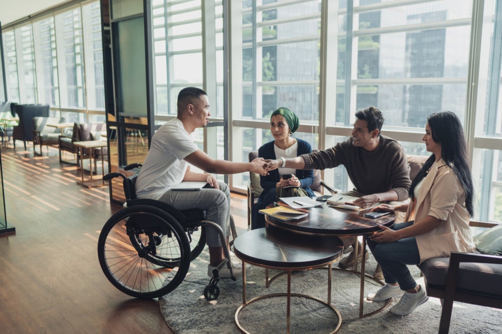 Three people in chairs and one person in a wheelchair sit around a table.