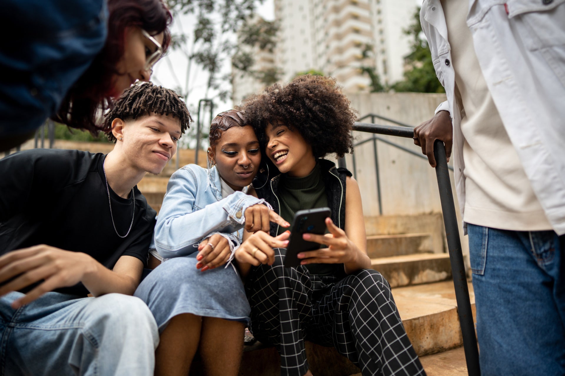 A group of teenagers gathered on a staircase look at a phone screen, representing digital wellbeing among youth.